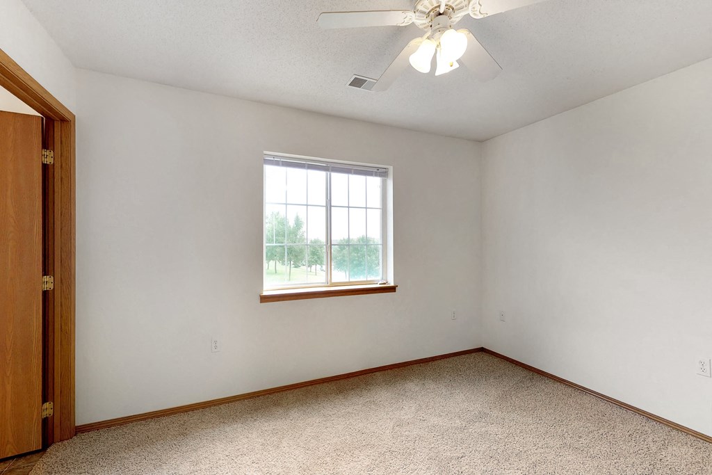 an empty bedroom with a window and a ceiling fan