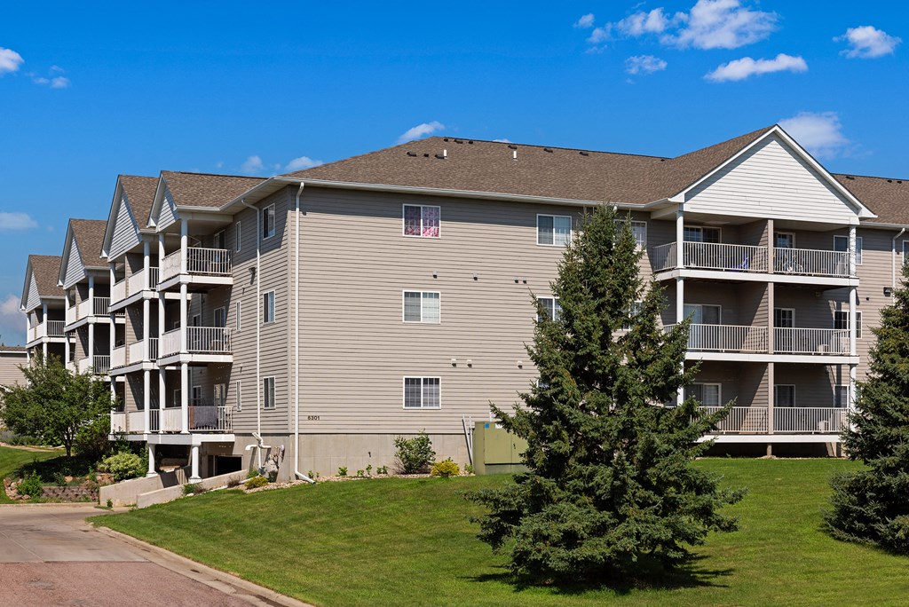 an exterior view of an apartment building with a tree in the grass