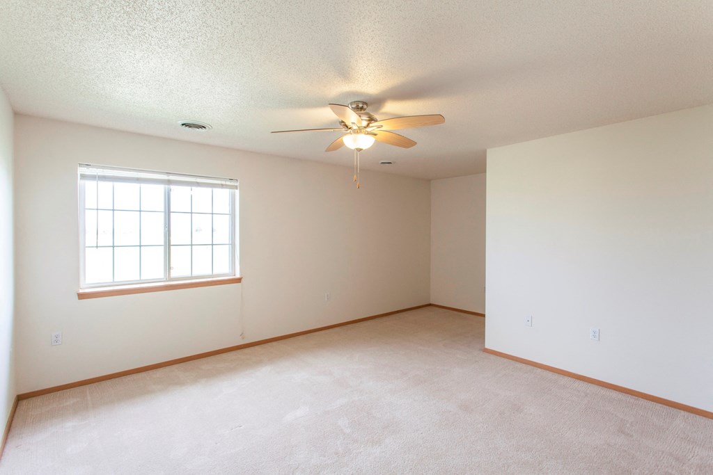 the spacious living room of an empty home with a ceiling fan