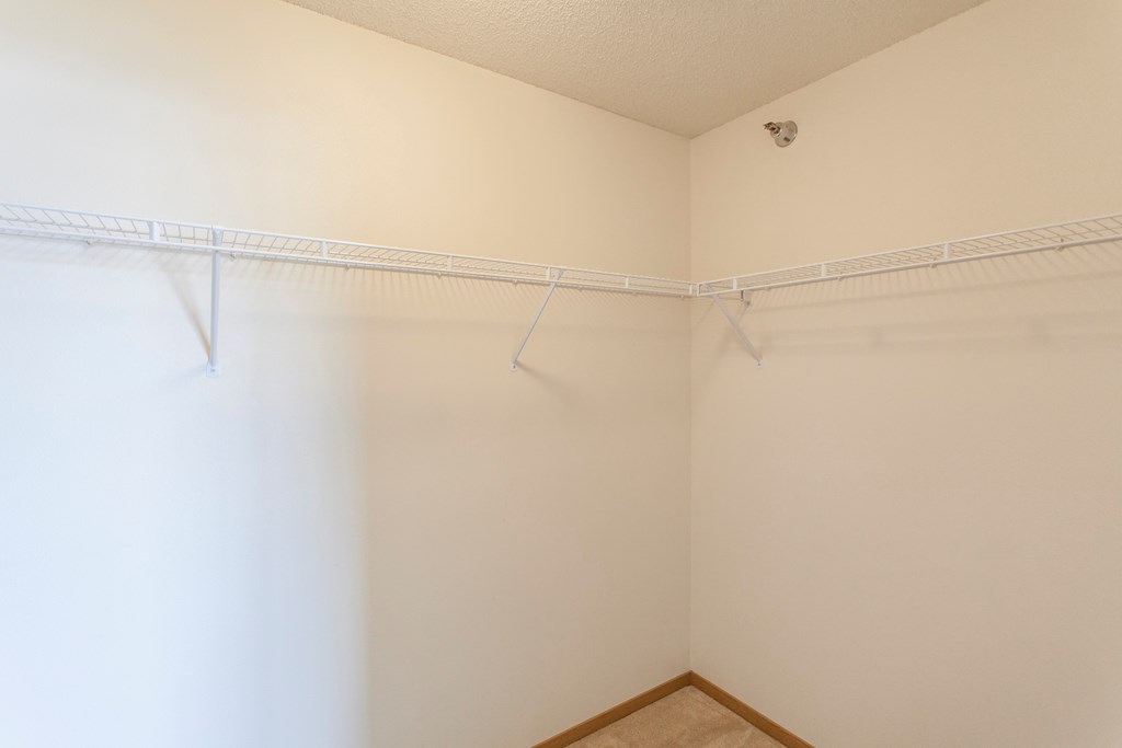 an empty closet in a white room with hanging rods on the wall