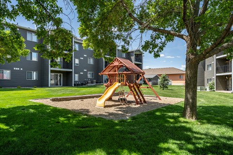 A playground with a slide and a wooden structure is surrounded by apartment buildings.