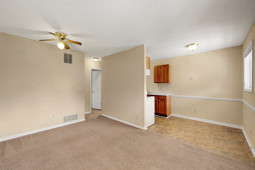 an empty living room with a ceiling fan and a kitchen