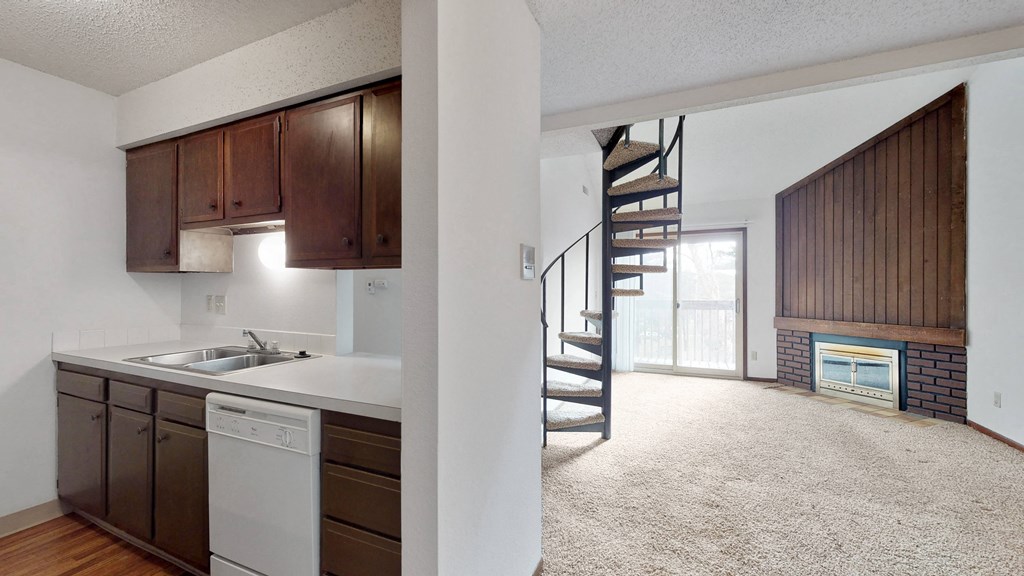 an open living room with a kitchen and a spiral stairway leading to a loft