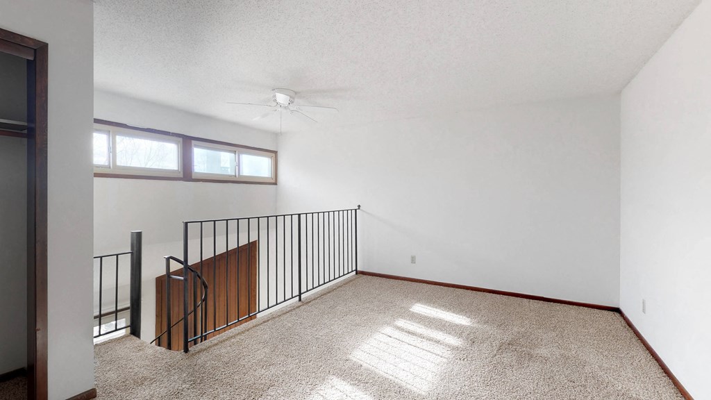 an empty living room with a balcony and a ceiling fan