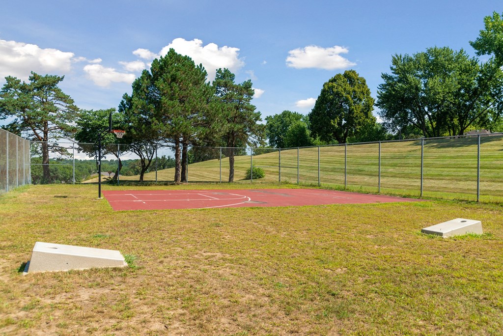 a basketball court in a park with a fence and trees