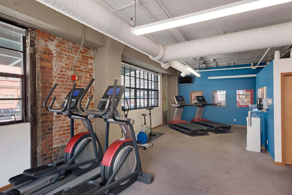 a gym with cardio machines and weights in a building with a brick wall