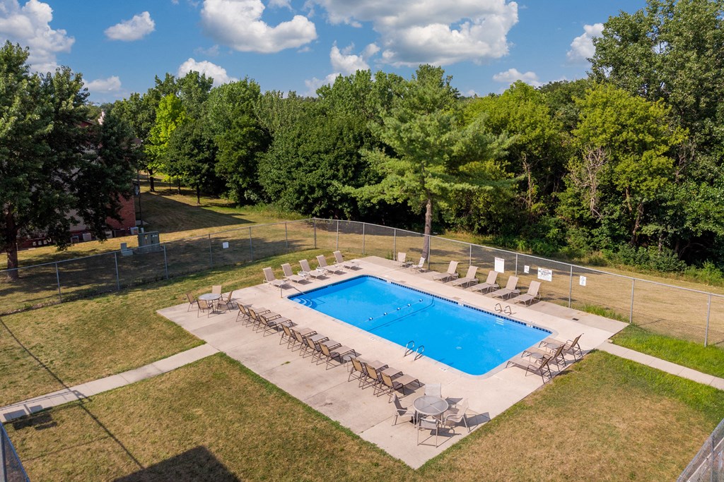 a swimming pool with chairs around it and trees in the background
