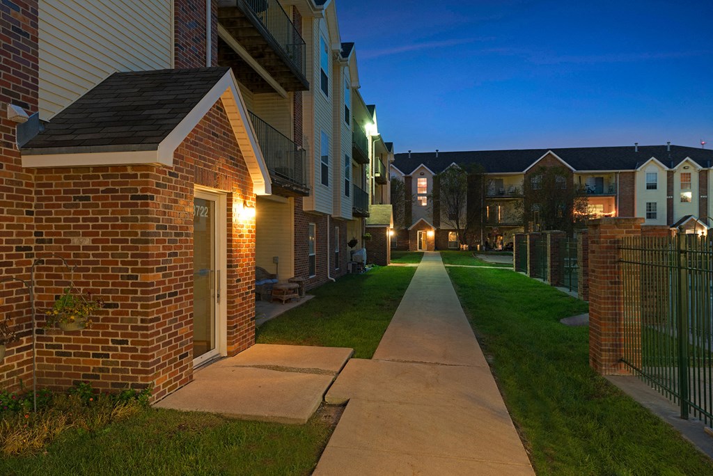 an empty sidewalk in front of an apartment building at night