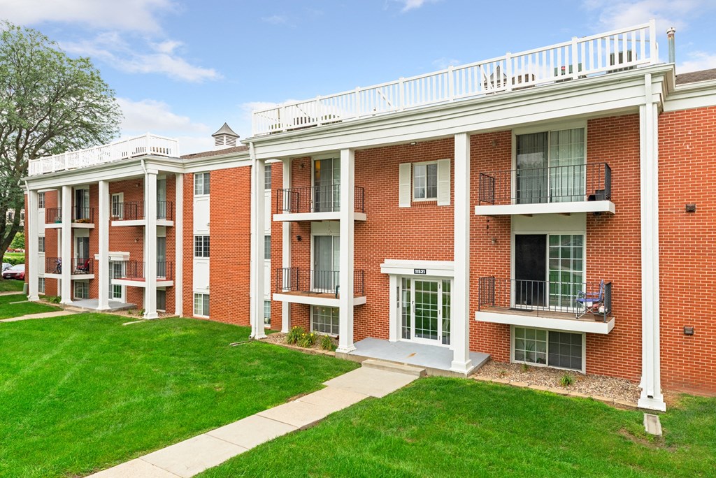 a red brick apartment building with green grass and a sidewalk