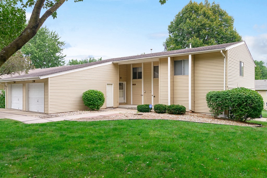 the front of a yellow house with a lawn and a driveway