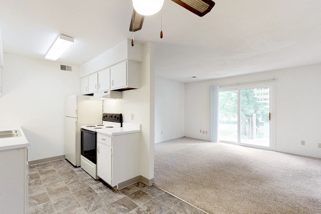 an empty living room with a kitchen with white cabinets and a window
