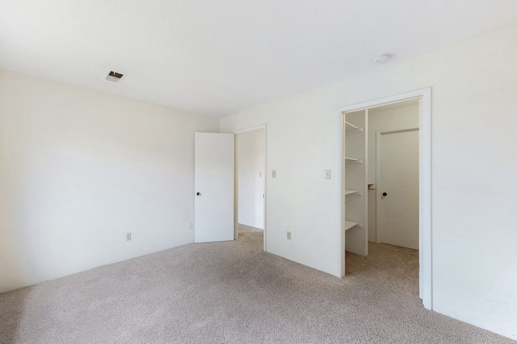 a bedroom with white walls and carpet and a closet