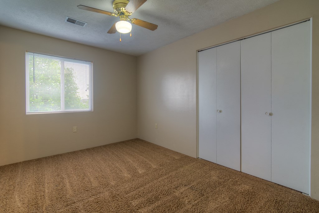 an empty bedroom with a ceiling fan and a window