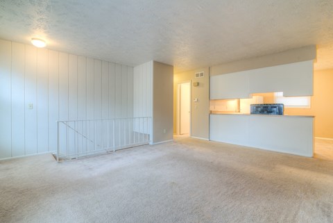 the living room and kitchen of an empty apartment with white walls and carpeting