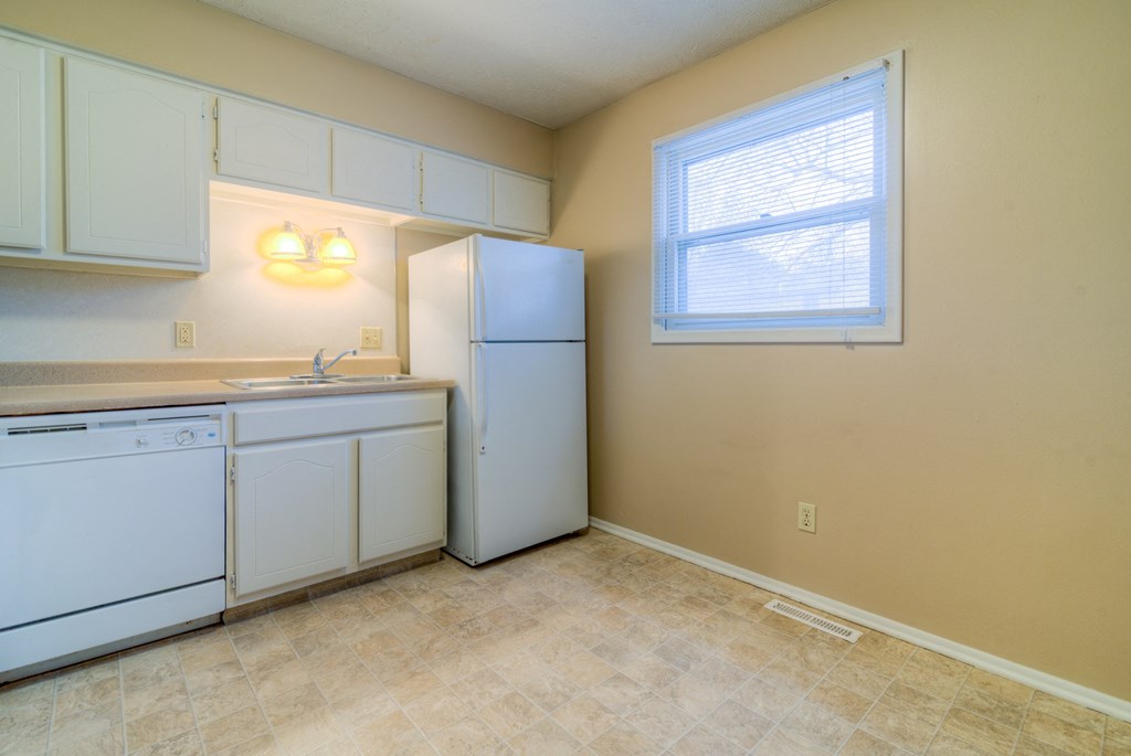 an empty kitchen with white appliances and a window