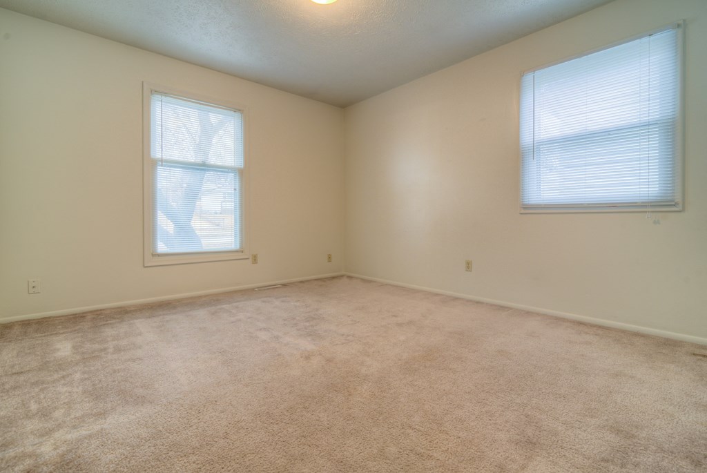 an empty living room with two windows and carpet