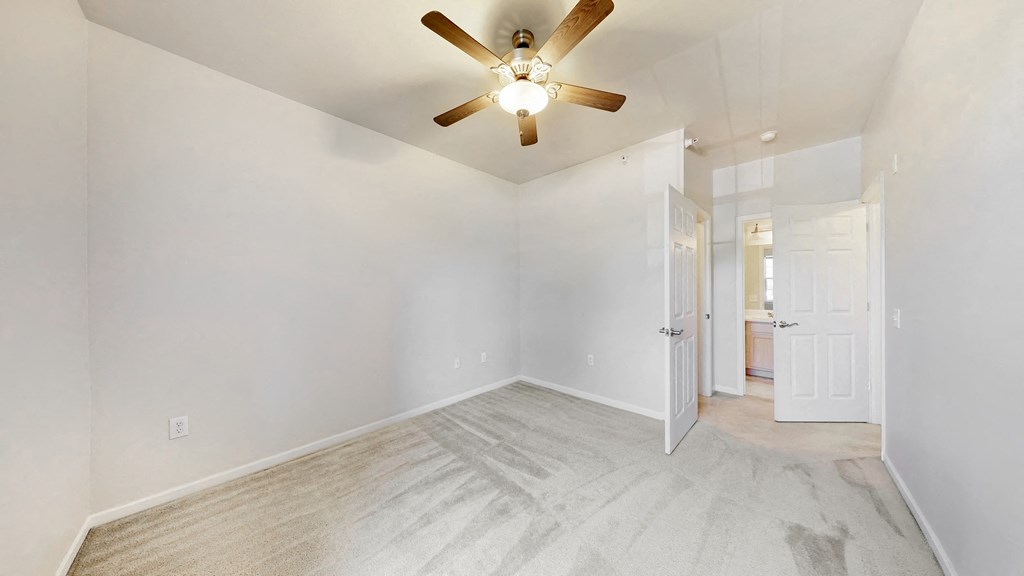 an empty bedroom with a ceiling fan and a door to a bathroom