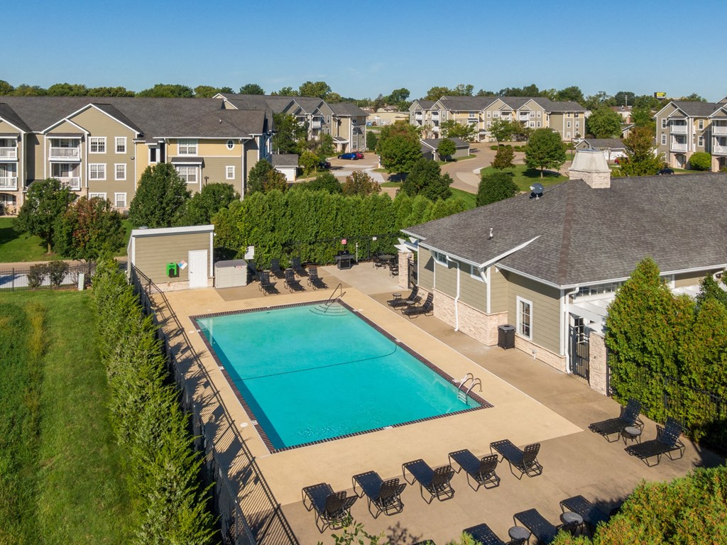 an aerial view of a swimming pool with chairs around it and apartments in the background