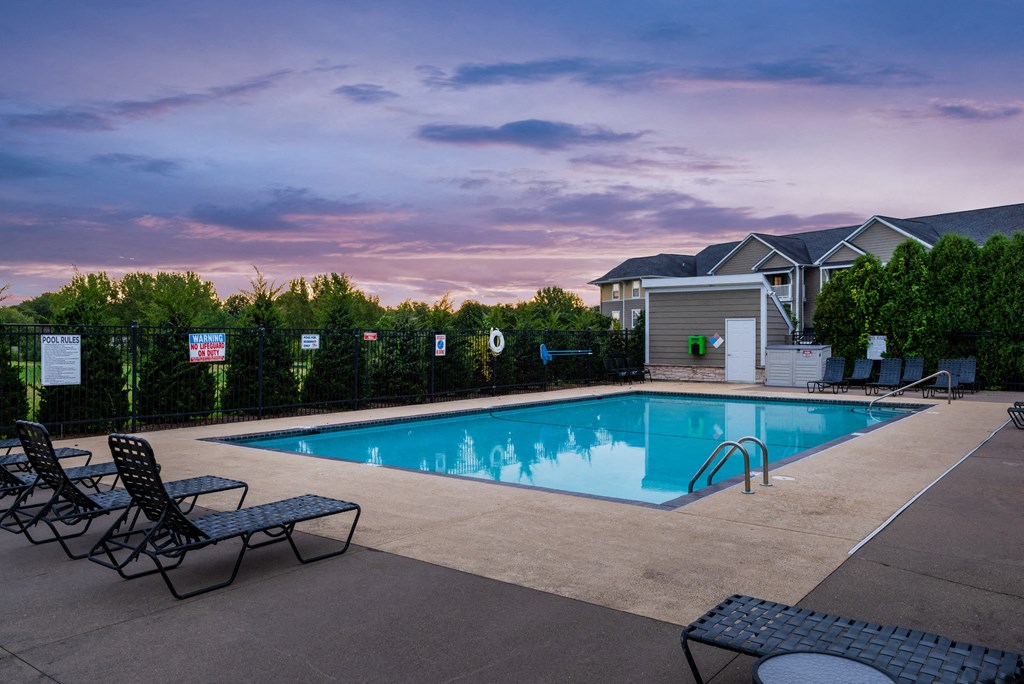 a swimming pool at sunset with chairs and a building