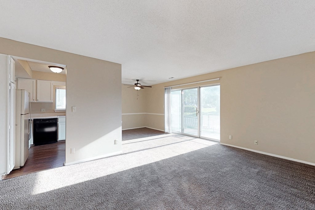 an empty living room with a sliding glass door to a kitchen