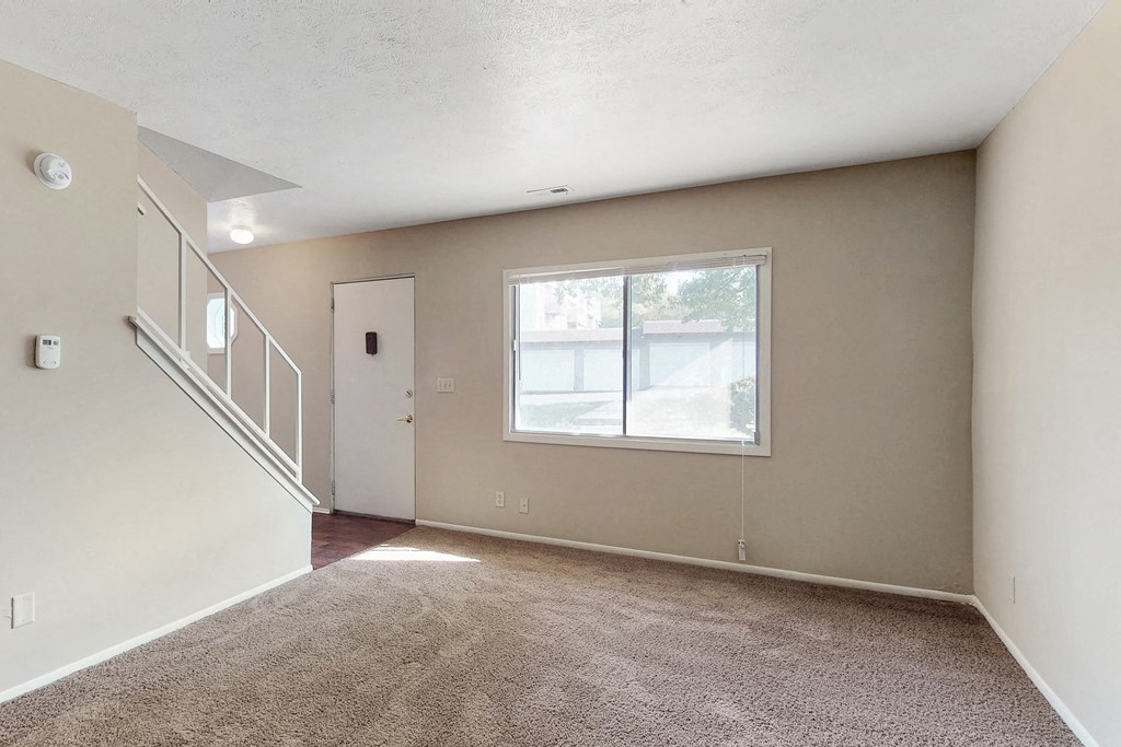 an empty living room with a large window and carpeted floors