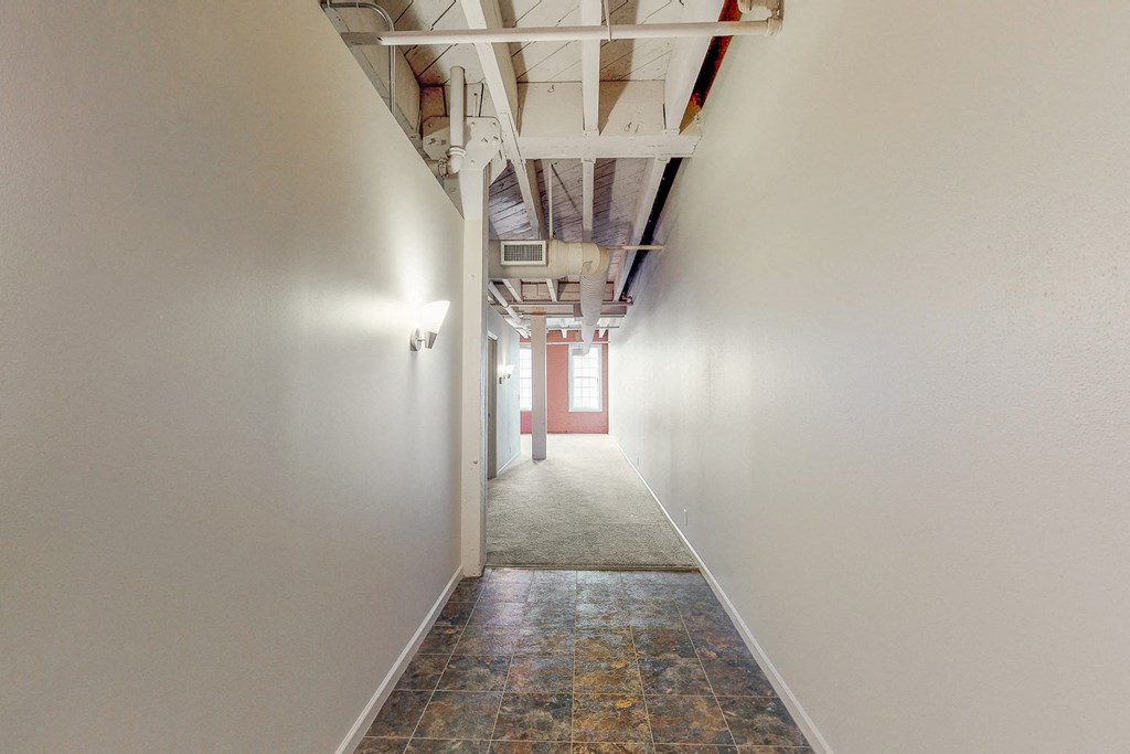 a hallway with white walls and a view of a red door