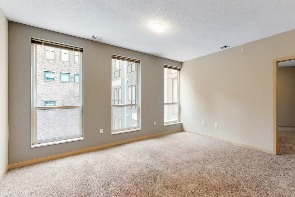 a living room with three windows and a carpeted floor