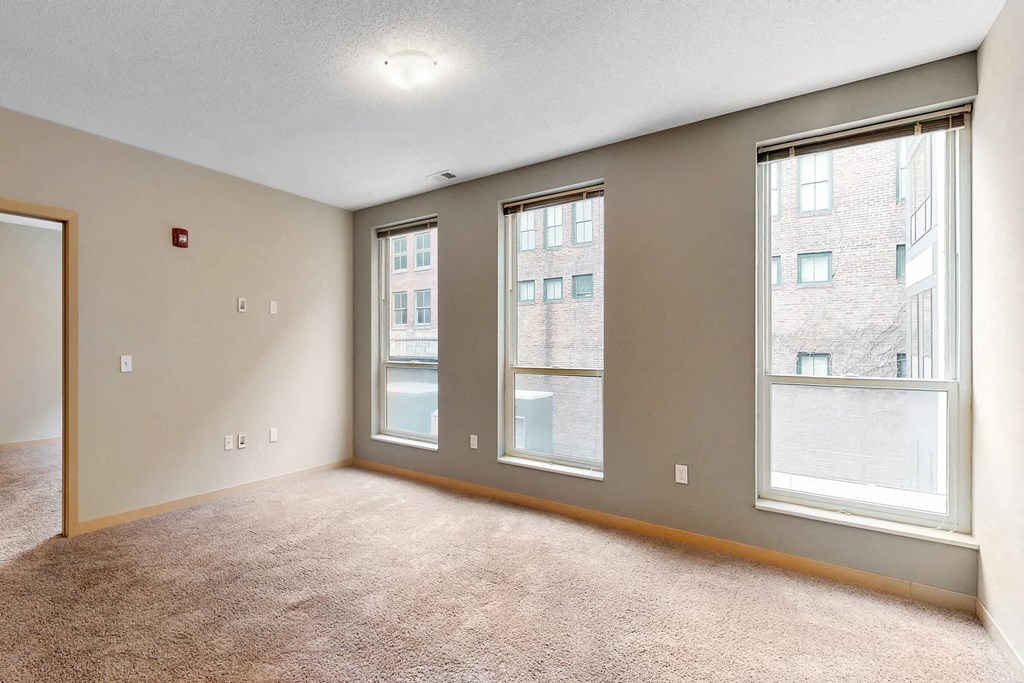 a living room with three windows and a carpeted floor