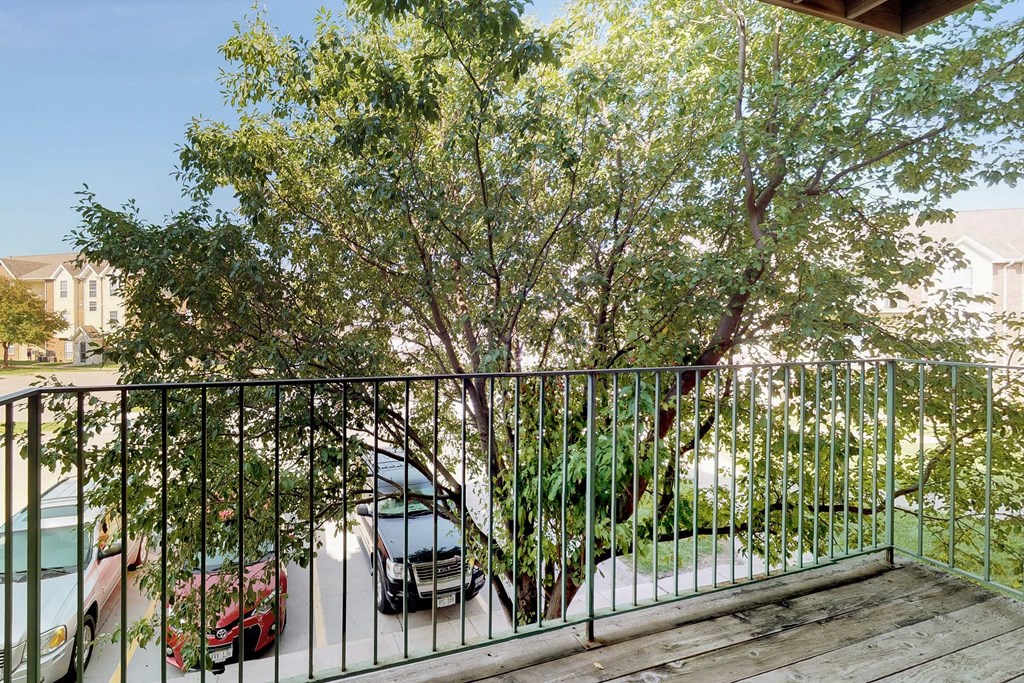 a balcony with a view of a tree and cars in a driveway