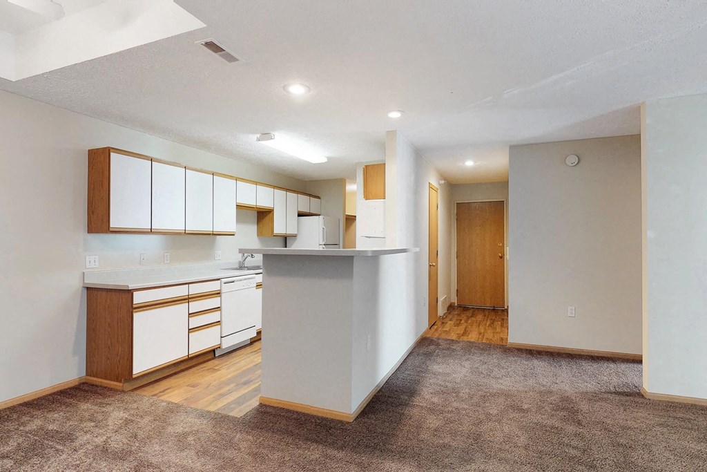 an empty living room with a kitchen with white cabinets