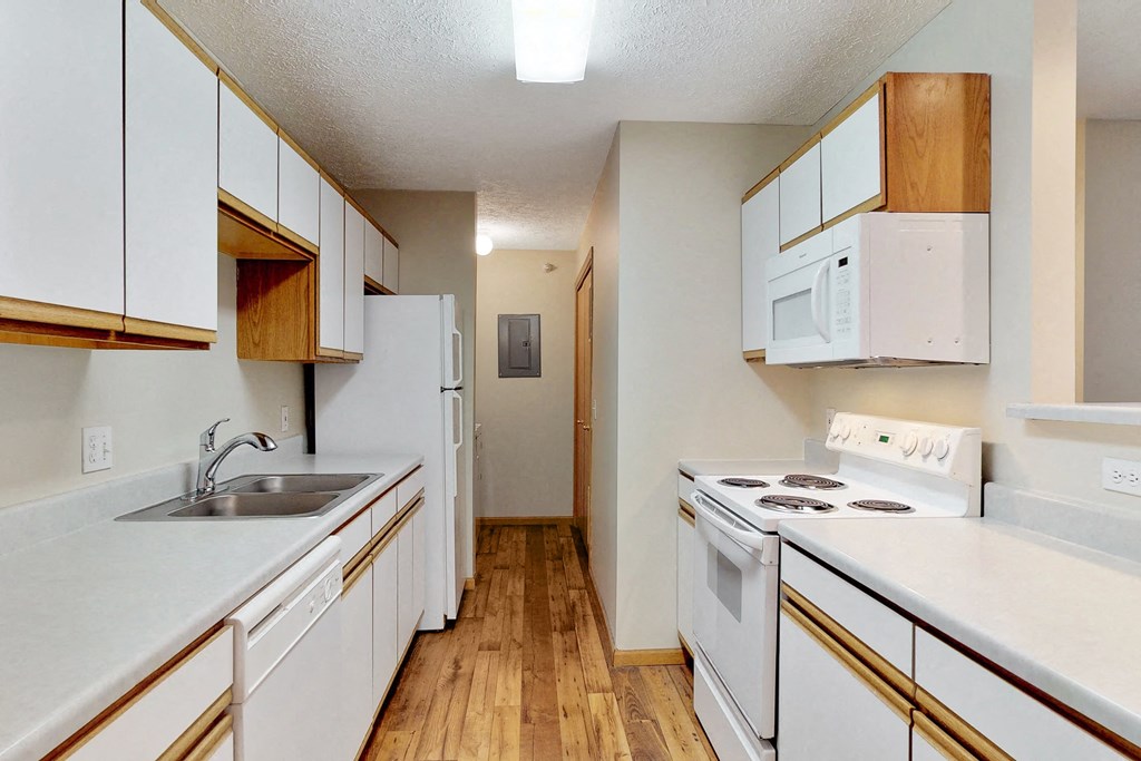 an empty kitchen with white appliances and wooden floors