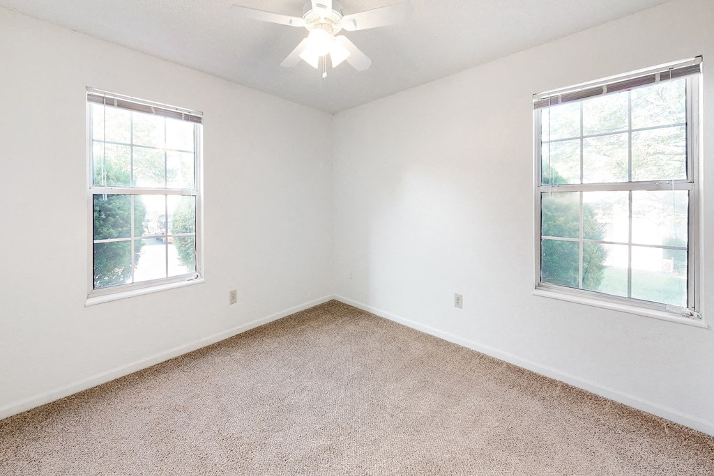 an empty bedroom with two windows and a ceiling fan