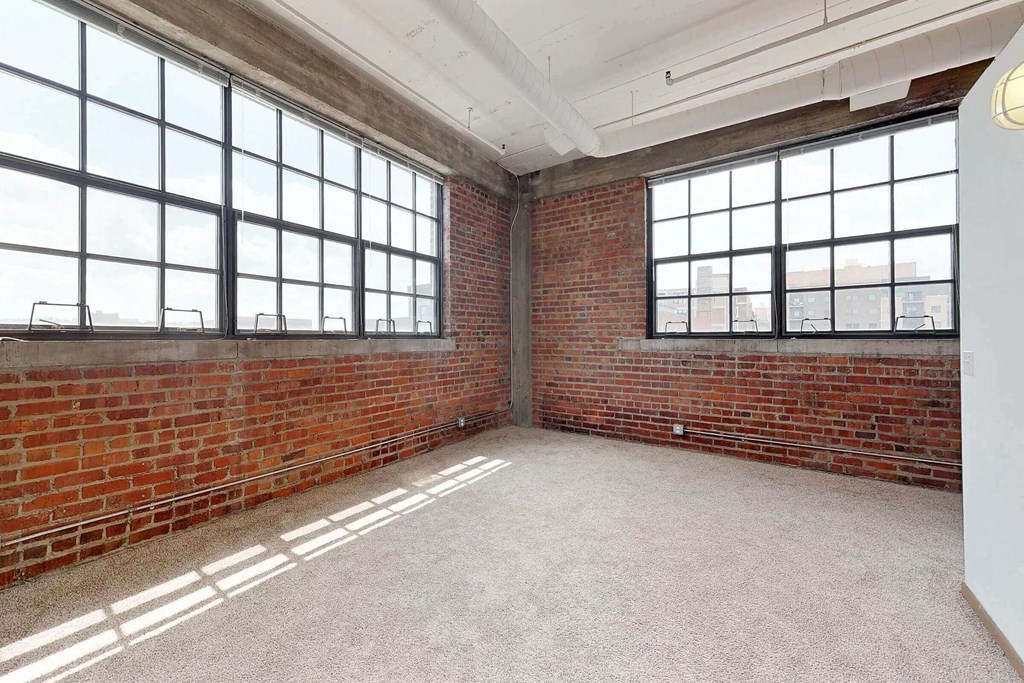 an empty room with a brick wall and large windows