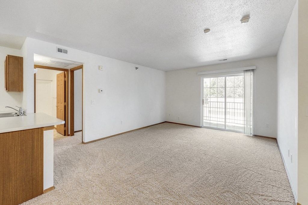 an empty living room and kitchen with a door to a balcony