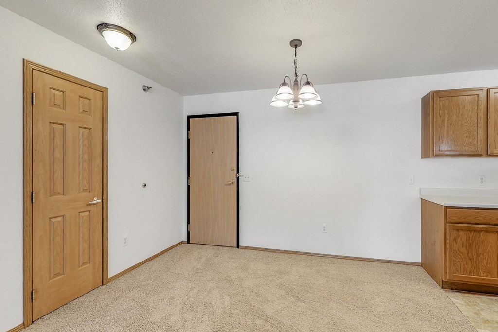 an empty living room with two doors and a kitchen