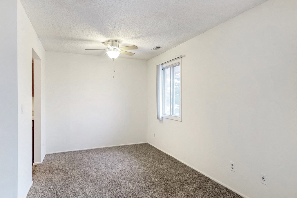 an empty living room with a ceiling fan and a window