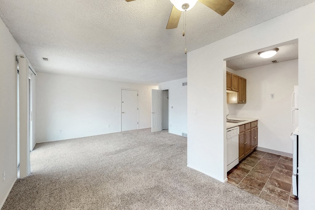 the spacious living room and kitchen with white walls and tile flooring