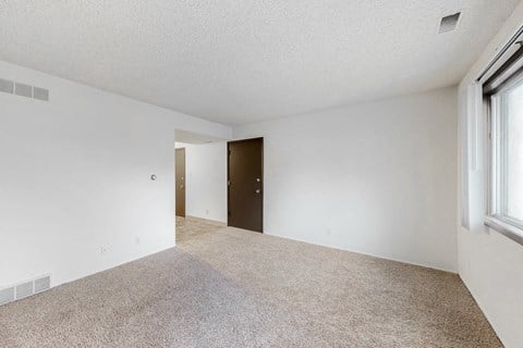 the spacious living room and dining room of an apartment with white walls and carpet