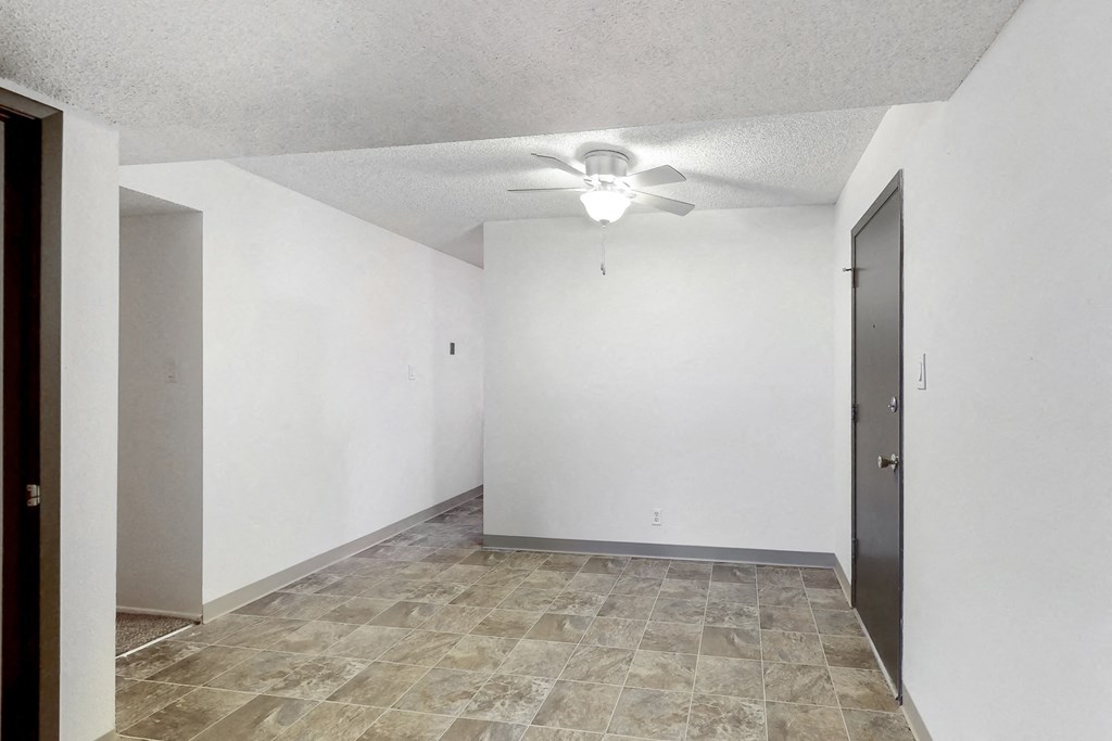 an empty living room with a ceiling fan and white walls