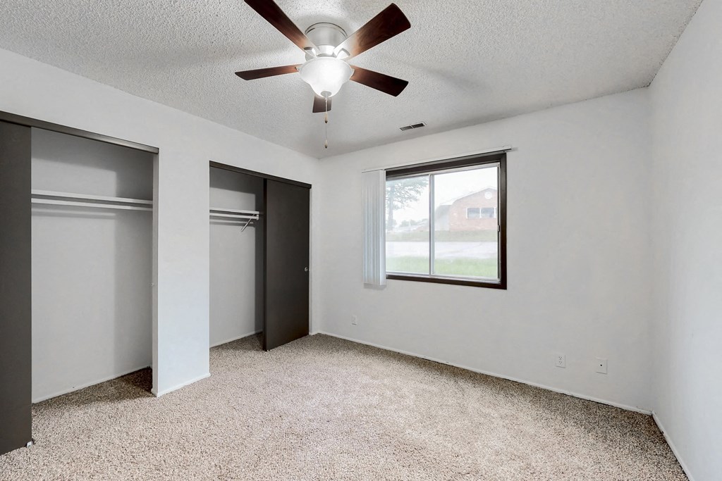 an empty living room with a ceiling fan and two closets