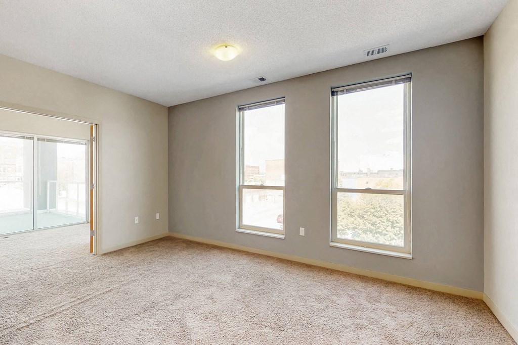 a living room with three windows and a carpeted floor