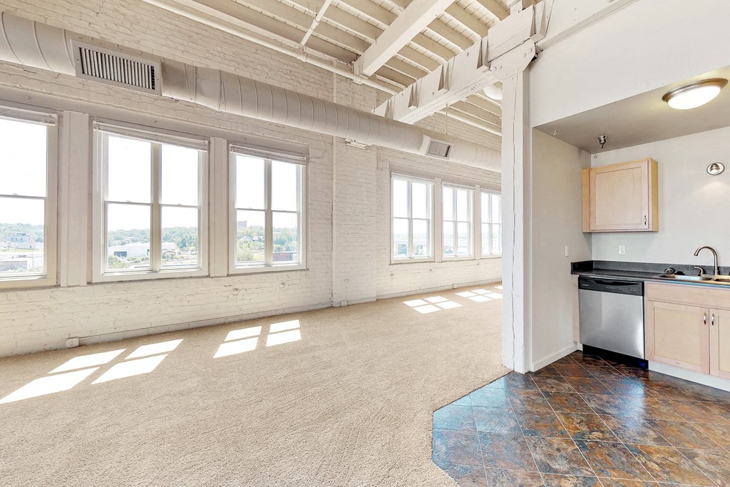 an empty living room with a kitchen and a large window