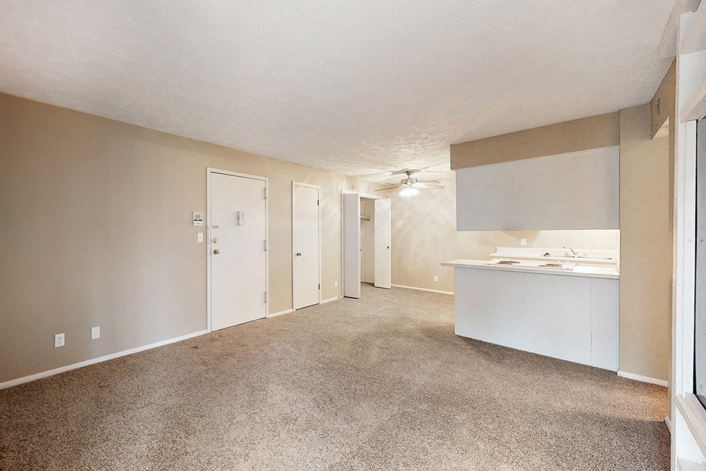 an empty living room with a kitchen and a ceiling fan