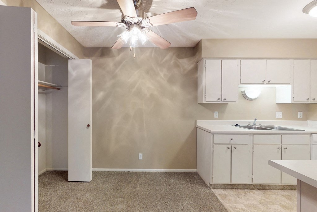 an empty kitchen with white cabinets and a ceiling fan