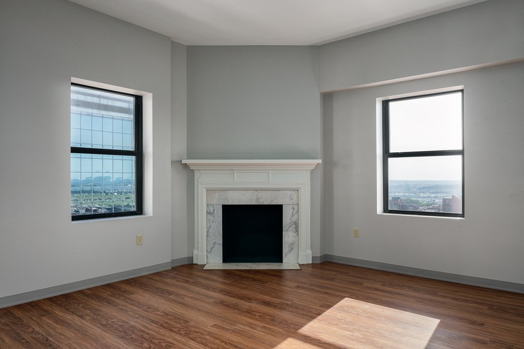 an empty living room with a fireplace and two windows
