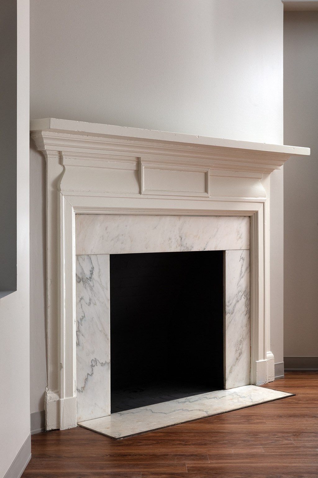a white marble fireplace in a living room with a wood floor