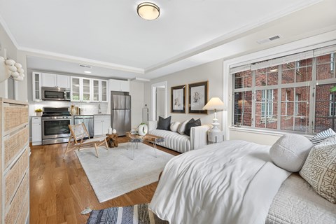 A well-lit bedroom with a large bed and a kitchen area in the background.