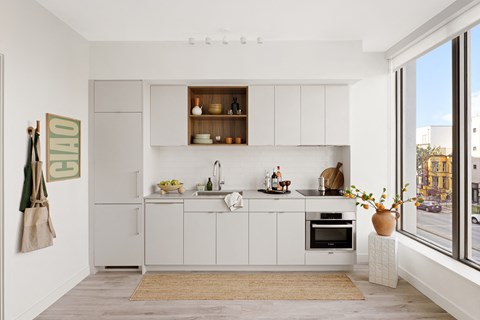 A modern kitchen with white cabinets and a wooden shelf above the sink.