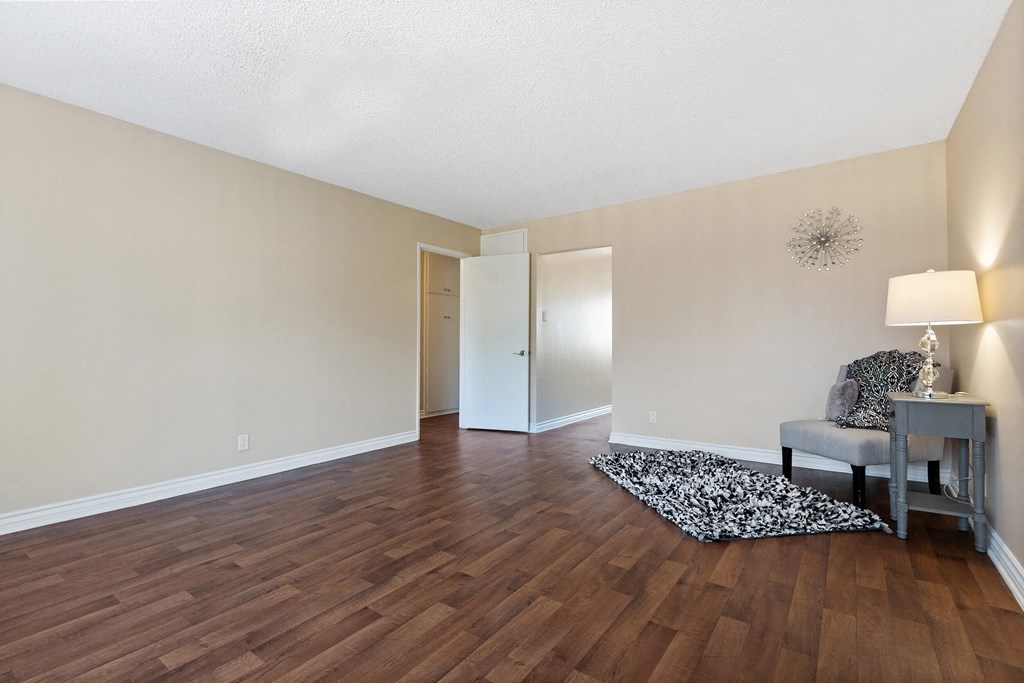an empty living room with hard wood flooring and a chair and table at Terramonte Apartment Homes, Pomona, California