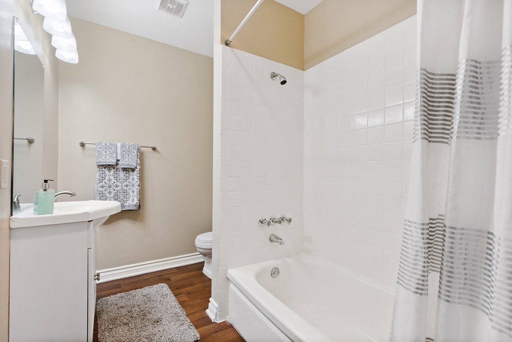 A bathroom with a white tub, sink and hardwood floors at Terramonte Apartment Homes, California